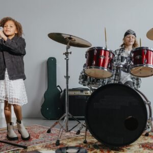 Two children performing in a music band with drums and microphone indoors.